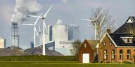 Idyllische niederländische Häuser im Vordergrund, grüner gepflegter Rasen. Im Hintergrund Kraftwerke und Windräder