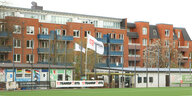 Ein Sportplatz, an dessen Rand eine Fahne mit der Aufschrift "Lukoil" weht, dahinter Wohnhäuser