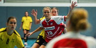 Umgeben von anderen Spielerinnen steht Cara Hartstock auf dem Handballfeld und hebt die Arme