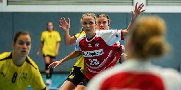 Umgeben von anderen Spielerinnen steht Cara Hartstock auf dem Handballfeld und hebt die Arme