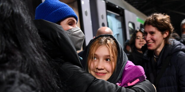 Eine Frau umarmt ein Mädchen, dahinter ein angekommener Zug