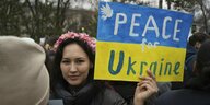 Frau mit einem blau-gelben Schild in der Hand. Darauf steht: Frieden für die Ukraine