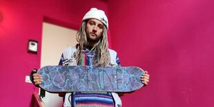 Ein junger Mann mit blonden Braids und Mütze steht mit einem Skateboard in der Hand auf einer Treppe. Auf dem Board steht "Ukraine"