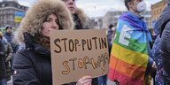 Menschen bei einer Demo, eine Person hält eine Pappe mit "Stop Putin, Stop War", jemand anderes trägt Pace-Fafhne