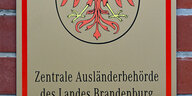 Das Foto zeigt das Schild am Eingang der Zentralen Ausländerbehrde in Eisenhüttenstadt mit dem Namen der Behörde unter dem brandenburgischen Wappen, dem roten Adler.