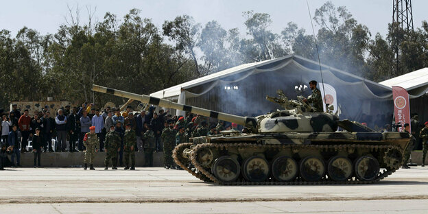 Ein libyscher Panzer rollt auf einer Straße vor im Hintergrund stehenden Menschen.