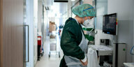 Eine Pflegemitarbeiterin in Schutzkleidung steht in einem Gang eines Krankenhauses
