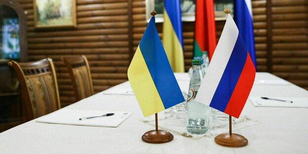 Eine Ukrinische und eine Russische Fahne sind auf einem Verhandlungstisch aufgestellt