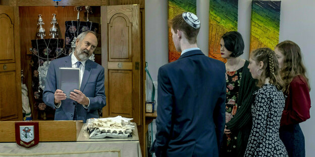 Ein Rabbi bei einer Bat Mitzwa in einer Synagoge. Vor ihm stehen eine Gruppe Jugendliche