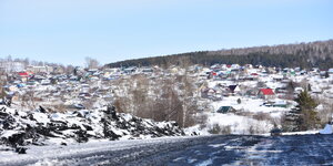Eine Straße in Sibirien, dreckig, im Hintergrund Häuser im Schnee auf einem Hügel