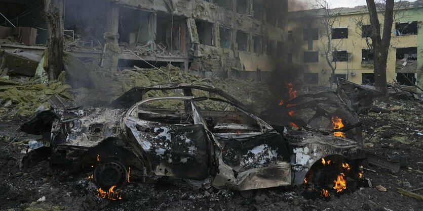 Ein Auto brennt vor der ausgebombten Ruine eines Gebäudes.