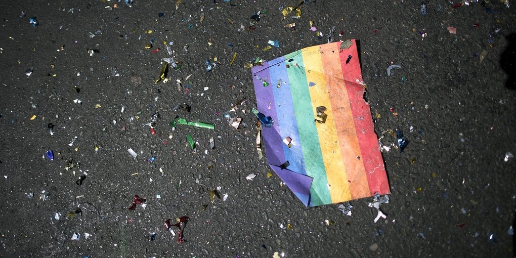 Ein REgenbogenfähnchen und buntes Konfetti liegen auf dem Asphalt