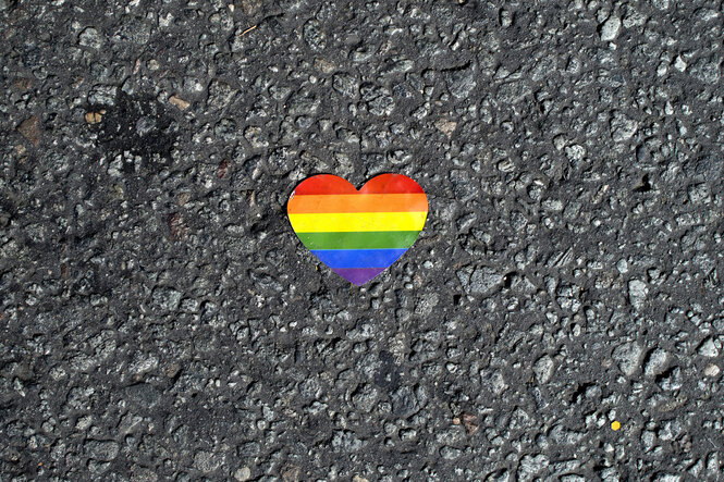 Ein Herz in Regenbogenfarben liegt auf dem Asphalt