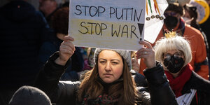 Eine Frau hält bei einer Demo ein Schild mit der Schrift Stop Putin-Stop War dahinter eine mit Krone maskierte Frau