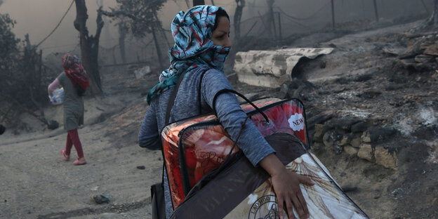 Eine Person mit Gepäck unter ihrem Arm in verbrannter Landschaft
