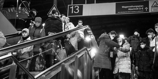 Schwarzweißfoto: Menschen auf einer Rolltreppe im Bahnhof