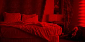 Ein in rotes Licht getauchtes Schlafzimmer. Hinter dem ungemachten Bett eine Tapete im Tiger-Look
