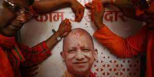 BJP Anhänger verteilen oranges Puder neben einem Plakat von Yogi Adityanath
