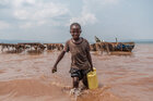 Ein Kind mit Kanister in der Hand steht in trübem Wasser