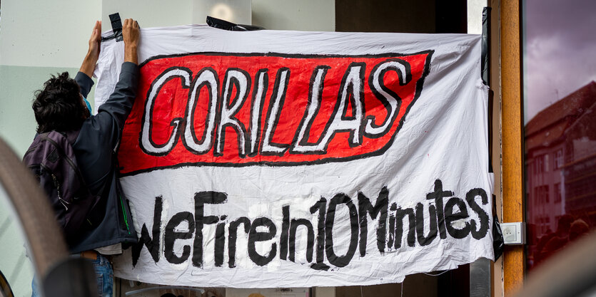 Ein Beschäftigter des Express-Lieferdiensts Gorillas klebt bei einer Demonstration vor der Firmenzentrale für bessere Arbeitsbedingungen ein Transparent mit der Aufschrift „Gorillas - We Fire in 10 Minutes“ an einer Wand fest.