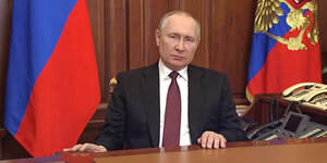 Wladimir Putin während seiner TV-Ansprache sitzend am Tisch, dahinter die russische Flagge