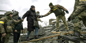 Soldaten helfen einer Frau, die einen Hund auf dem Arm hält, Trümmer zu überqueren