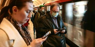 Menschen warten auf die U-Bahn und schauen auf ihr Handy