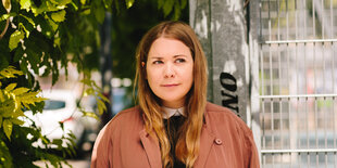 Schriftstellerin Stefanie Sargnagel in Jacke unter Baum mit grünen Blättern