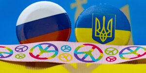 Buttons mit der russischen und der ukrainischen Fahne, davor ein Band mit Peace-Zeichen