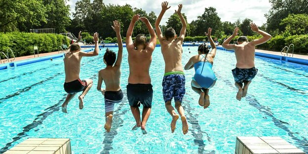 Sechs Kinder und Jugendliche springen gleichzeitig vom Beckenrand in einem Freibad ins Wasser