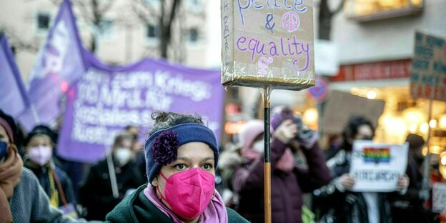 Eine Frau trägt eine pinke Mundschutzmaske und hält ein Plakat hoch