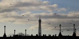 Menschen gehen über eine Brücke, im Hintergrund d er Eiffelturm