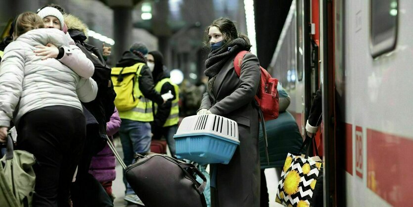 Eine Frau steigt aus dem Zug und hält eine Transportbox für Tiere in der Hand