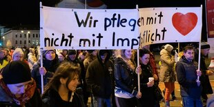 Proteste gegen die Impfpflicht: Menschen halten ein Banner auf dem steht: "Wir pflegen mit Herz, nicht mit Impfpflicht"