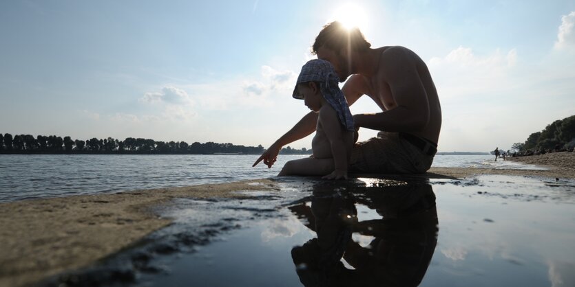 Ein Vater sitzt mit seinem Kind am Strand