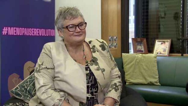 Grauhaarige Frau sitzt in einem Sessel, hinter ihr der Schriftzug Menopauserevolution Grauhaarige Frau sitzt in einem Sessel, hinter ihr der Schriftzug Menopauserevolution
