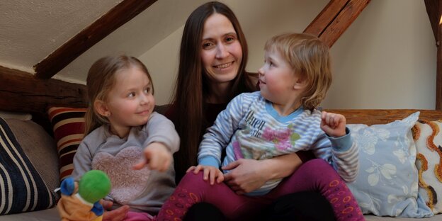Eine Frau sitzt mit zwei Kleinkindern auf einem Sofa Eine Frau sitzt mit zwei Kleinkindern auf einem Sofa