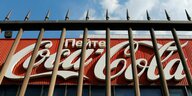 Durch einen Zaun sieht man das Coca-Cola-Logo mit kyrillischer Schrift darüber