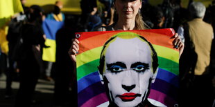 Eine Person mit einem Transparen, auf dem Putin mit Regenbogenfarben abgebildet ist.