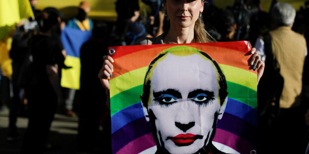 Eine Person mit einem Transparen, auf dem Putin mit Regenbogenfarben abgebildet ist.