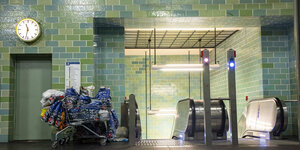 Ein Einkaufswagen mit vielen Plastiktüten in einem U-Bahnhof vor einer Rolltreppe