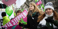 Zwei Demonstrantinnen auf einem Anti-CETA-Protest. Im Hintergrund sieht man Transparente und ein Schwein, auf dem steht "Stop TTIP"