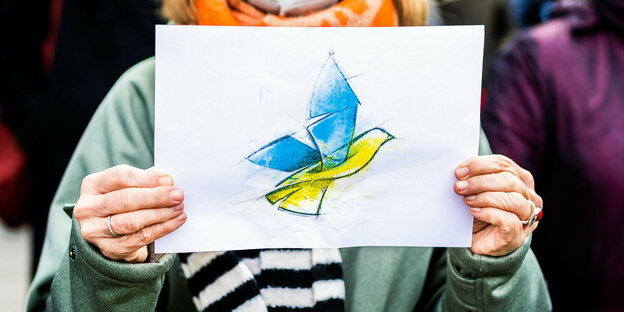 : Die Abbildung einer Friedenstaube in den ukrainischen Landesfarben ist auf dem Plakat einer Demonstrantin