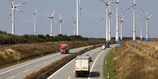 Lkw auf einer Autobahn, im Hintergrund sind Windräder zu sehen