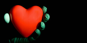 ein rotes Herz in einer Hand, die medizinische Handschuhe trägt