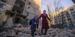 Eine Frau läuft mit einem Kind über Trümmer