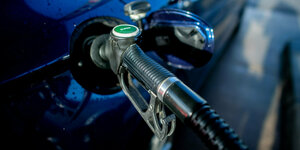 : Eine Zapfpistole mit der Aufschrift ·Super· steckt an einer Tankstelle in der Tanköffnung eines Fahrzeugs.