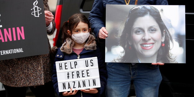 Ein kleines Mädchen hält ein Schild hoch, auf dem "Free Nazanin" steht, neben mir hält ein Mann ein Plakat mit Nazanins Gesicht hoch.