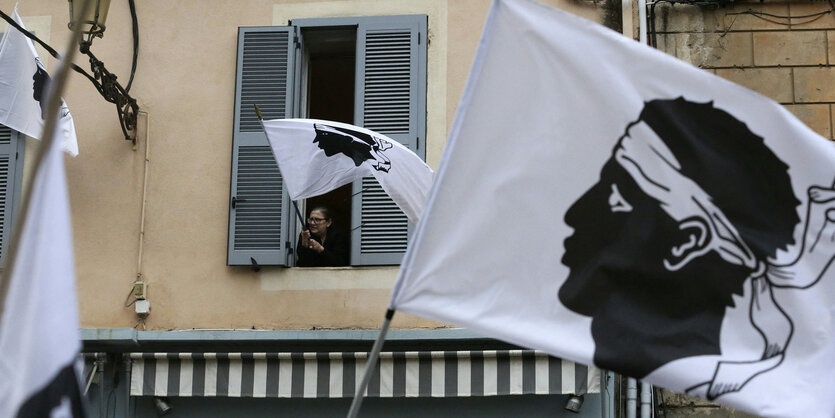 Eine Frau hisst die Fahne mit korsischem Emblem.