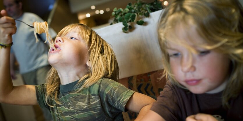 Zwei Kinder sitzen im Restaurant und essen Spaghetti